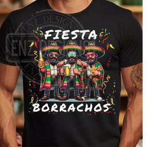 May include: Black t-shirt featuring a graphic of three men in sombreros, holding drinks. The text "Fiesta Borrachos" is displayed above and below the image. The men are wearing colorful serape jackets.