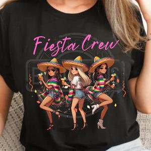 May include: Black t-shirt featuring the text "Fiesta Crew" in pink script above an illustration of three women in sombreros, holding cocktails. They wear colorful serapes and denim shorts, celebrating.