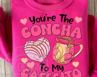 May include: Pink sweatshirt with the text "You're the Concha to my Cafecito" in white. The design features a pink heart-shaped pastry and a brown and yellow mug with a floral design.