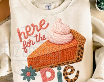 May include: Cream-colored sweatshirt with a graphic of a pie slice and the text "here for the pie." The pie slice has a knitted texture with orange and brown colors, topped with pink whipped cream. A blue and pink flower and the word "Pie" are also featured.