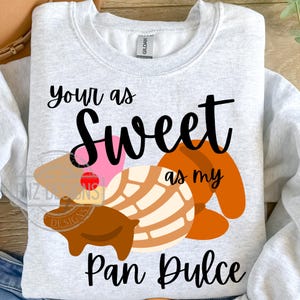 May include: A gray sweatshirt with the text "Your as sweet as my Pan Dulce" in black. The text is surrounded by a graphic of a brown pig, a pink and white pastry, and an orange pastry.