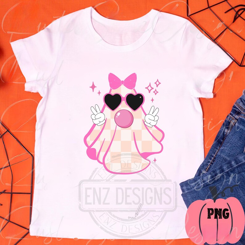 Op de afbeelding: Wit T-shirt met een roze spook dat een zonnebril en een strik draagt. Het spook heeft een geruit patroon en houdt vredestekens vast. De tekst "ENZ DESIGNS" staat op het T-shirt.