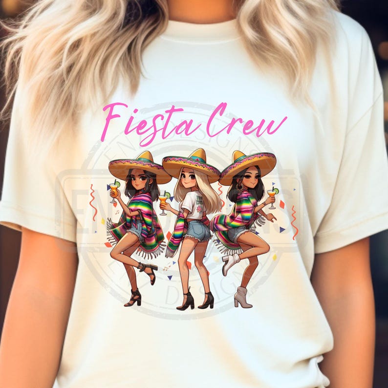 May include: A cream-colored t-shirt featuring the text "Fiesta Crew" in pink script. The graphic depicts three women in sombreros, holding cocktails, and wearing colorful serapes and denim shorts. The design has a festive, celebratory theme.