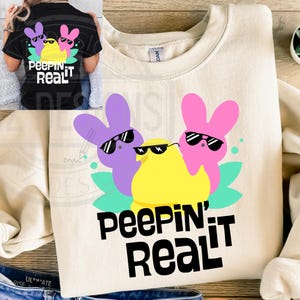 May include: A light beige sweatshirt with a graphic of three pastel-colored marshmallow peeps wearing sunglasses. The peeps are surrounded by green leaves. The text "Peepin' It Real" is printed in black below the graphic.