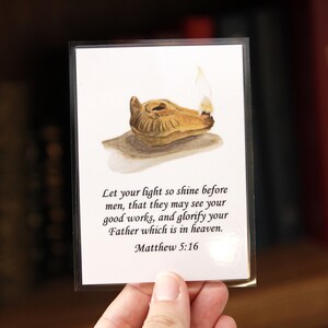 May include: A card featuring a watercolor illustration of an oil lamp with a flame. The card includes the text "Let your light so shine before men...Matthew 5:16."