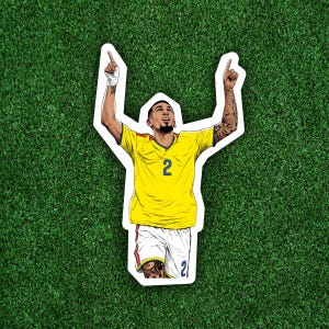 May include: A die-cut sticker featuring a cartoon illustration of a soccer player with a goatee, wearing a yellow jersey with the number 2 in blue, and white shorts with the number 2 in blue. The player has both arms raised with index fingers pointing up.