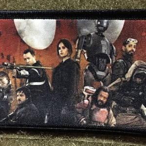 May include: A rectangular patch with a black border features a group of characters from a science fiction film. The image shows a diverse group of people, including a robot, against a backdrop of red and white. The patch is likely for a jacket or bag.