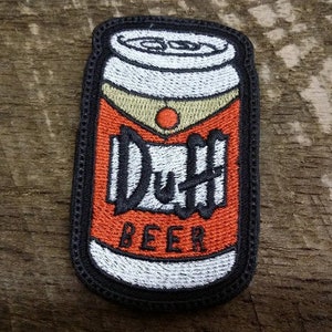 May include: A black and white embroidered patch of a can of Duff Beer. The can is orange and white with the words "Duff Beer" in black.