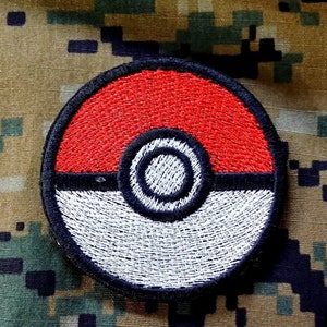 May include: A red, white, and black embroidered patch depicting a Pokeball, a circular object with a red top, a white bottom, and a black center ring.