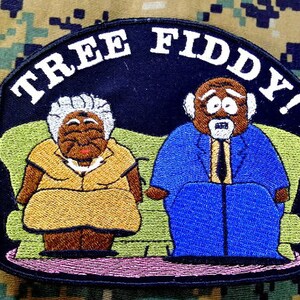 Op de afbeelding: Gestikt patch met een cartoon-koppel dat op een bank zit. Het patch is zwart met witte tekst die "TREE FIDDY!" luidt.