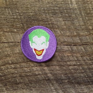 May include: Purple embroidered patch with a green and white Joker face. The Joker is smiling with a wide, toothy grin.