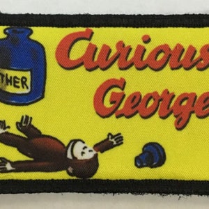 May include: A yellow fabric patch with black stitching around the edges. The patch features a cartoon monkey lying on its back with a blue bottle labelled "ETHER" and the text "Curious George" in red.