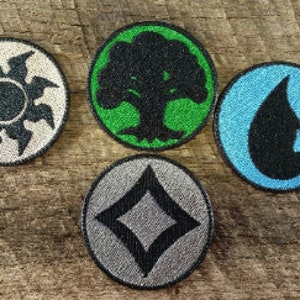 Può includere: Sei toppe rotonde ricamate con diversi simboli che rappresentano i cinque elementi della magia nel gioco Magic: The Gathering. I simboli sono fuoco, acqua, terra, aria e un teschio nero.
