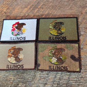 Peut inclure: Quatre écussons rectangulaires avec le sceau de l'État de l'Illinois. Les écussons ont différentes couleurs de fond : blanc, vert olive, beige et camouflage. Chaque écusson porte le mot "ILLINOIS" brodé en couleur foncée.