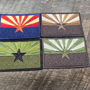 May include: Four embroidered patches featuring the Arizona state flag design. Each patch has a rectangular shape with a star and sunburst design. The color schemes include blue, brown, green, and a combination of red, yellow, and orange.