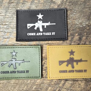 Könnte beinhalten: Drei rechteckige Aufnäher mit Stern- und Gewehrmotiv und dem Text "COME AND TAKE IT". Die Aufnäher sind schwarz, olivgrün und beige. Das Gewehr und der Stern sind weiß, silber und braun.