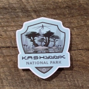 May include: A blue and gray shield-shaped sticker with the text "KASHYYYK NATIONAL PARK" and a stylized image of a forest with trees and a creature in the sky.