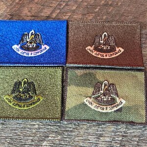 May include: Four embroidered patches in blue, brown, olive green, and camouflage. Each patch features a pelican emblem with the text "Union, Justice & Confidence" in a curved banner. The patches are square-shaped.