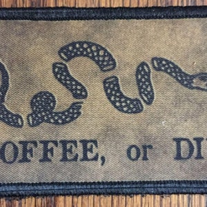 Puede incluir: Un parche de tela marrón con un diseño de serpiente negra y el texto "COFFEE, or DIE".