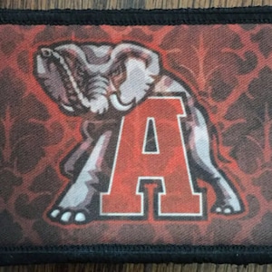 Peut inclure: Un patch brodé rouge et blanc avec un éléphant et la lettre "A" sur un fond à motifs rouge et noir.