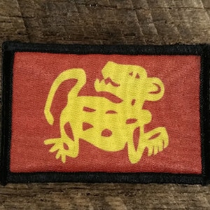 May include: A red fabric patch with a yellow stylised animal design. The animal is a jaguar or a similar feline.