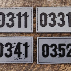 May include: Four rectangular gray patches with black raised numbers. The top left patch displays 0311, the top right displays 0331, the bottom left displays 0341, and the bottom right displays 0352. Each patch features a stitched border.