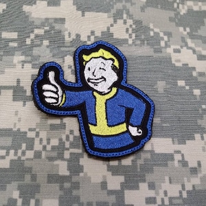 May include: A blue and yellow embroidered patch of a cartoon character giving a thumbs up. The character has blonde hair and is wearing a blue jumpsuit.