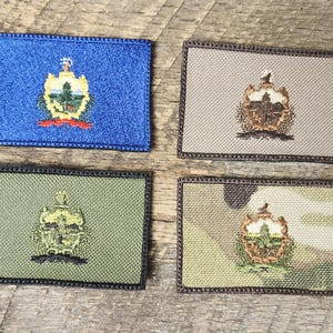 May include: Four rectangular embroidered patches with a state seal design. The patches are in blue, tan, olive green, and camouflage patterns. Each patch has a black border and features a detailed emblem.