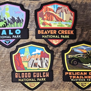 May include: Four shield-shaped patches featuring colorful illustrations of fictional landscapes and vehicles. The patches are labeled Halo National Park, Beaver Creek National Park, Blood Gulch National Park, and Pelican Drop Trailhead Warthog Tours.