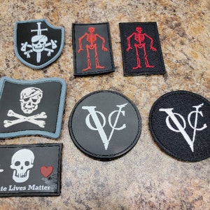 May include: A set of nine embroidered iron-on patches featuring various pirate and skull designs. The patches are black, white, red, and blue. The patches include a skull and crossbones, a skeleton, a pirate flag, and a skull with a heart. The text "Pirate Lives Matter" is on one of the patches.