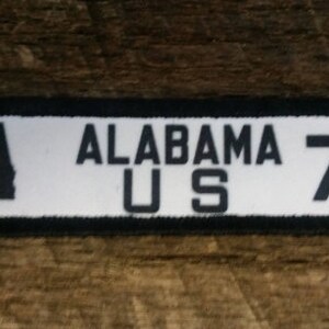 May include: White patch with black border and text "ALABAMA US 72" and a black outline of the state of Alabama.