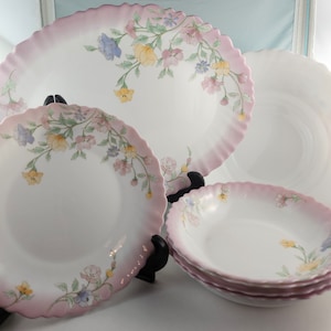 May include: Set of six white ceramic plates with a pink rim and floral design. The plates feature a delicate floral pattern in shades of pink, yellow, and blue.