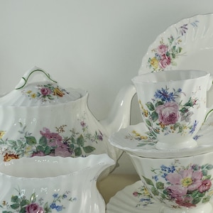 May include: A white tea set with floral designs. The set includes a teapot, creamer, sugar bowl, cup, and saucer. The floral designs are in shades of pink, yellow, blue, and green.
