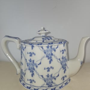 May include: A white teapot with a blue floral pattern. The teapot has a lid with a knob on top and a spout on the side. The teapot is decorated with a delicate blue floral design.
