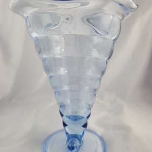 May include: A light blue glass vase with a wide, flared opening and a spiral design. The vase has a blue rim and a round base.