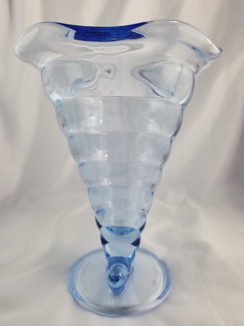 May include: A light blue glass vase with a wide, flared opening and a spiral design. The vase has a blue rim and a round base.