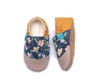 Può includere: Due scarpine per bambini con un motivo floreale su sfondo blu navy. Le scarpe hanno la punta in pelle scamosciata beige e i talloni giallo senape. Il motivo floreale comprende fiori rosa e dettagli bianchi. Scarpe per neonati.