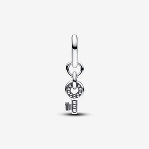 May include: A silver-toned metal charm featuring a vertical key design. The key has a circular head with a series of small, raised circular indentations around the center, and a rectangular shaft with horizontal grooves, suspended from a ring.