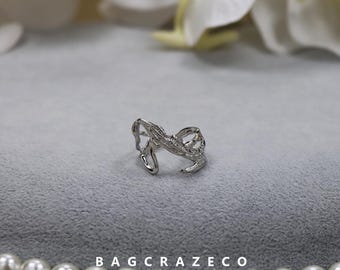 May include: A silver ring featuring a delicate, intricate design. The ring is set with small, clear stones and has a unique, organic shape.