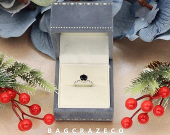 Könnte beinhalten: Ein Ring mit einem schwarzen Edelstein, einem silbernen Band und einem zarten floralen Design. Der Ring wird in einer blauen Samt-Ringbox präsentiert.