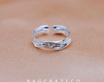 May include: A silver adjustable ring with a wavy, organic design. The ring is handcrafted and has a minimalist aesthetic.