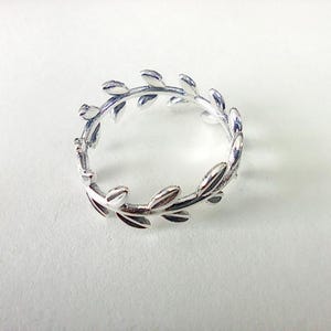 May include: A silver ring with a leaf design. The ring is shaped like a wreath, with small, detailed leaves encircling the band. The ring is displayed on a white background.