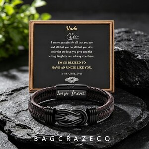 Könnte beinhalten: Ein dunkelbraunes geflochtenes Lederarmband mit einem schwarzen Metallverschluss in Form eines Unendlichkeitsknotens und einem Magnetverschluss mit der Gravur Love you forever, präsentiert mit einer Karte mit dem Text Uncle.
