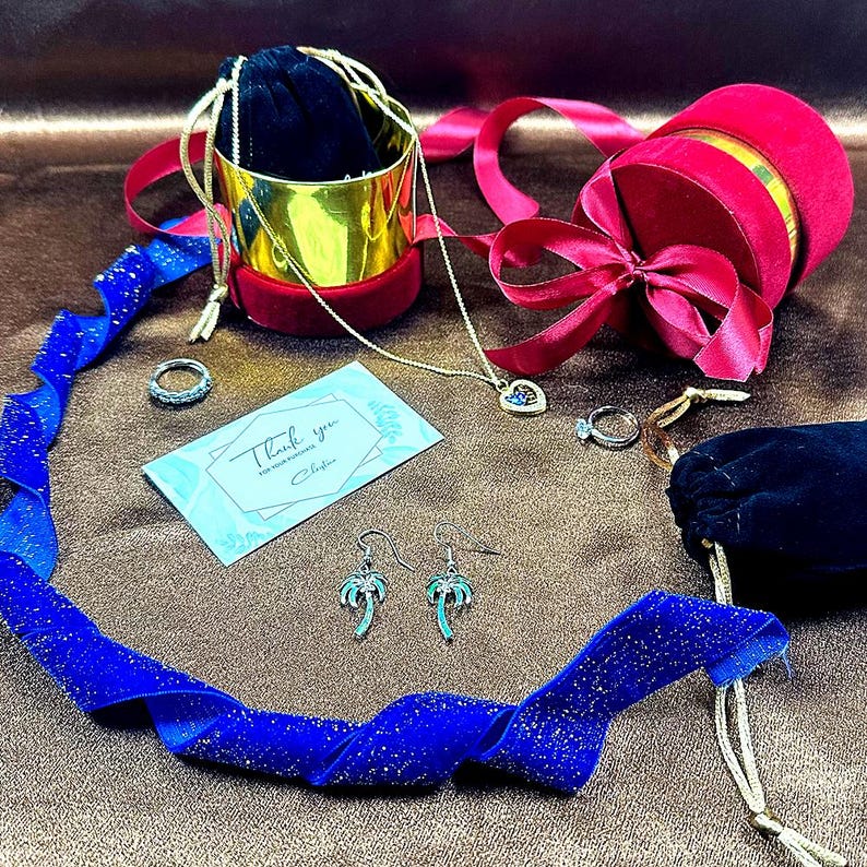 May include: A gift box set with a red velvet box, a gold box, a blue velvet ribbon, a necklace with a heart pendant, a pair of palm tree earrings, a ring, and a card that says "Thank you for your purchase".