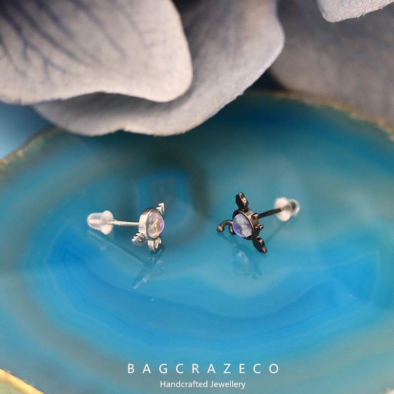 May include: Two silver earrings with a moonstone gemstone and a silver post. The earrings are on a blue background.