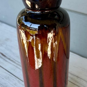 May include: A tall, ceramic vase with a glossy finish. The vase features a dark brown, ruffled rim and a body with vertical stripes of red, brown, and gold. The vase is approximately 10 inches tall.