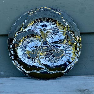 May include: A round, silver-toned metal serving tray featuring a three-section design. Each section is embossed with a detailed, radiating leaf or floral pattern that extends from a central point, finished with a scalloped, decorative edge.