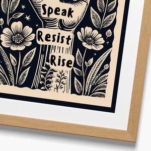 May include: Black and white print of a raised fist with the words "Speak", "Resist", and "Rise" written on it. The fist is surrounded by stylized flowers and leaves on a cream background.
