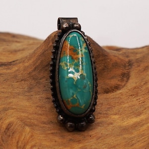 May include: A silver pendant with a green and brown oval turquoise stone set in a beaded border.
