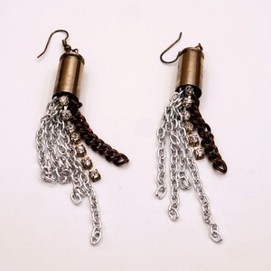 May include: A pair of silver and brown chain earrings with a bullet casing charm and rhinestones.